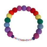 A handmade rainbow felt beaded bracelet with a personalized name section spelling 'NELLY [heart] WARREN' using letter tiles, displayed on a white marble background.